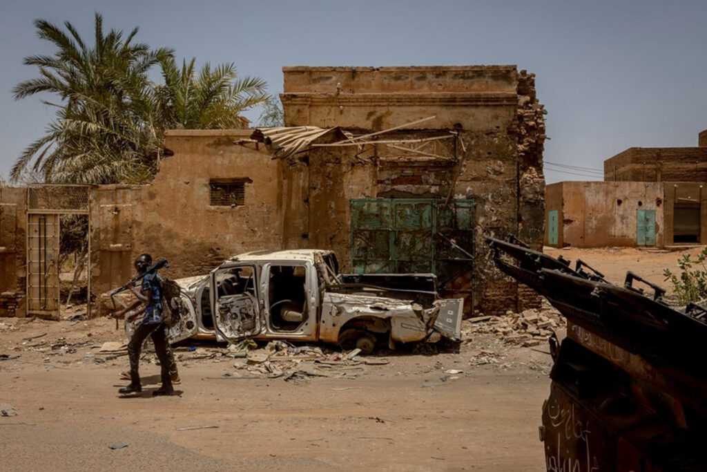 Sudanese Armed Forces soldiers walk through a road lined with destroyed buildings in Al-Shaabi market, liberated from RSF control in March 2024.